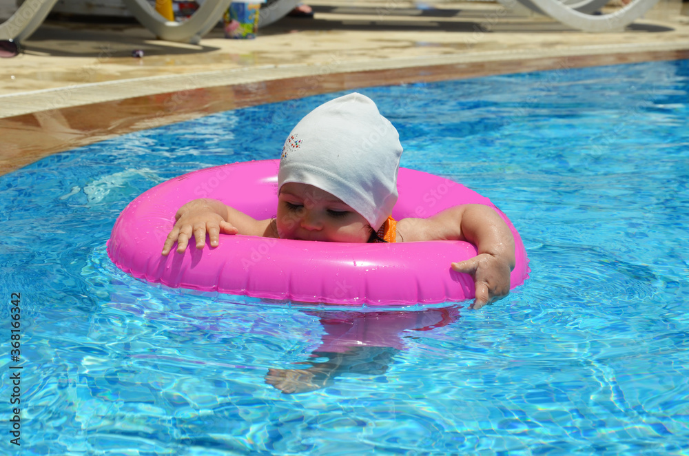 Portrait of happy white Caucasian child baby girl toddler in swimming pool outdoor. training to float with pink inflatable circle ring in water. Healthy active lifestyle. summer, joy, vacation