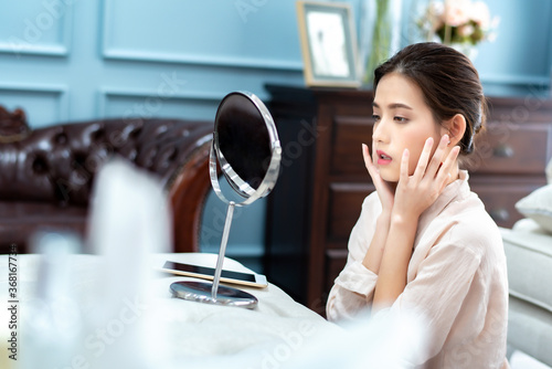 Fototapeta Naklejka Na Ścianę i Meble -  Portrait of beautiful charming young Asian woman looking her face in mirror to checking facial at living room in the morning. Happiness relaxation mood concept.