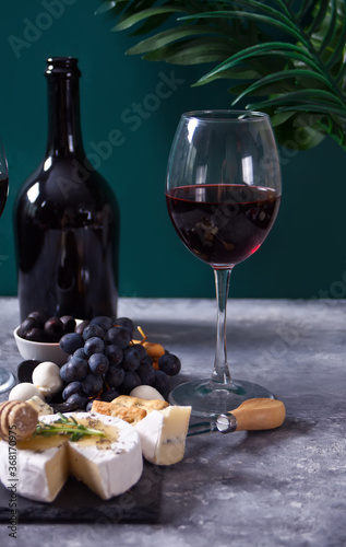 glass of red wine and plate with assorted cheese, fruit and other snacks for party