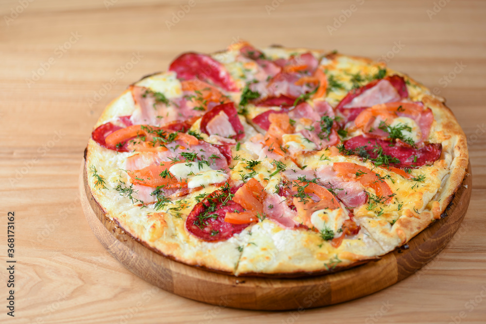 Fresh pizza with tomatoes, cheese and mushrooms on wooden board over rustic wooden table background closeup.
