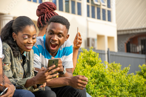 group of excited young africans feeling excited while looking at a mobile phone  sitting with friends