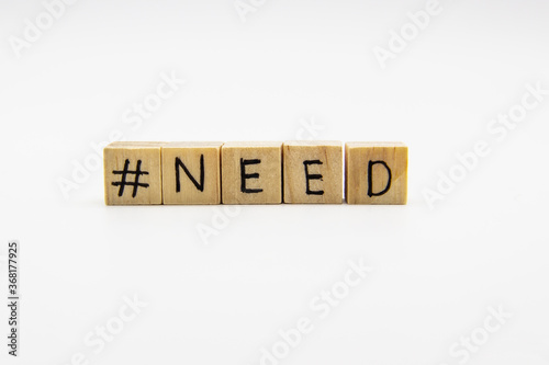 A word NEED with hashtag. Wooden small cubes with letters isolated on white background with copy space available. Concept image with hashtag.