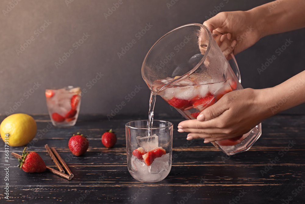 Woman pouring fresh strawberry lemonade in glass on table - obrazy, fototapety, plakaty 