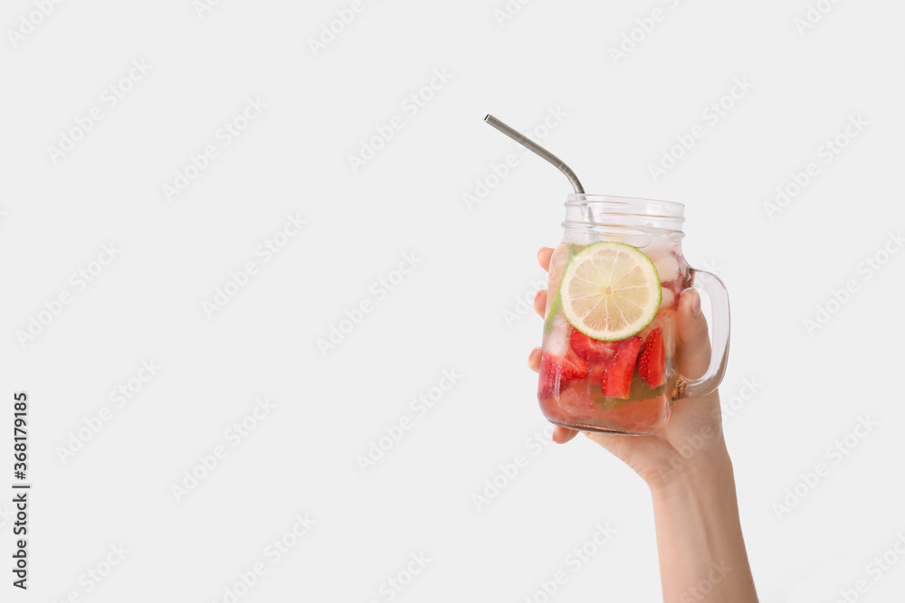 Hand with mason jar of fresh strawberry lemonade on light background - obrazy, fototapety, plakaty 