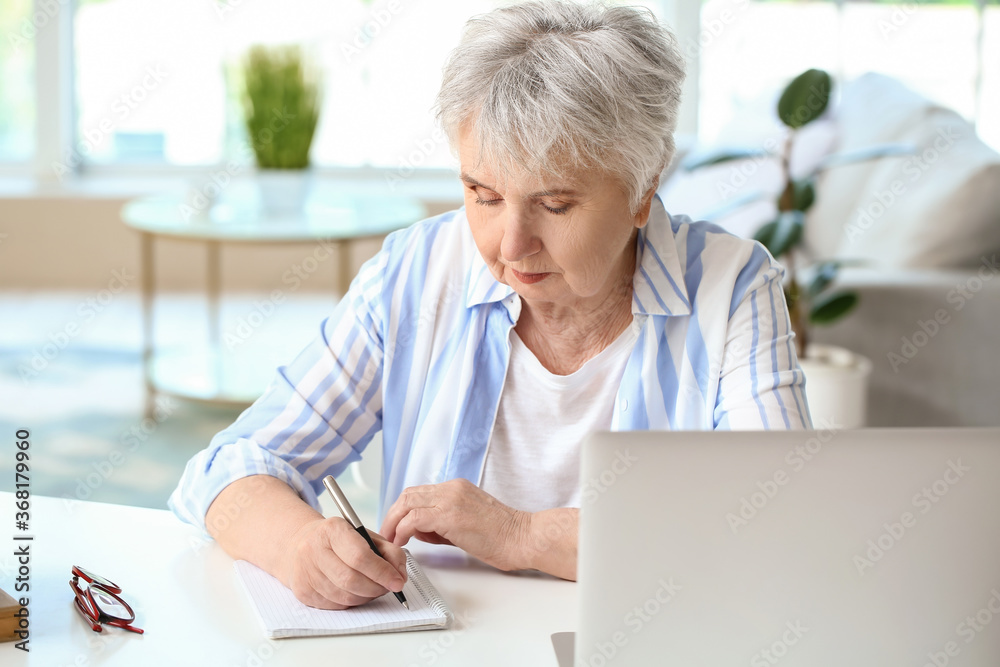 Senior woman writing in notebook at table Senior woman writing in notebook at table