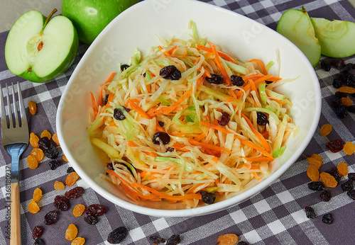 Sauerkraut with carrots and raisins in a deep dish. On a napkin, sliced apples and scattered raisins.