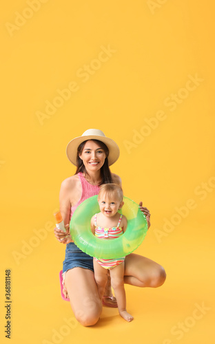 Mother and her little daughter with sunscreen cream and inflatable ring on color background © Pixel-Shot