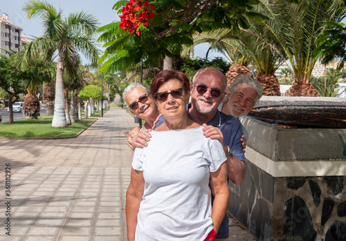 Cheerful group of senior friends having fun in public park - four retired people under palms trees and blossom plants - active retirement concept