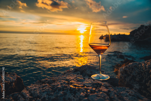 glass of wine at rocky sea beach on sunset