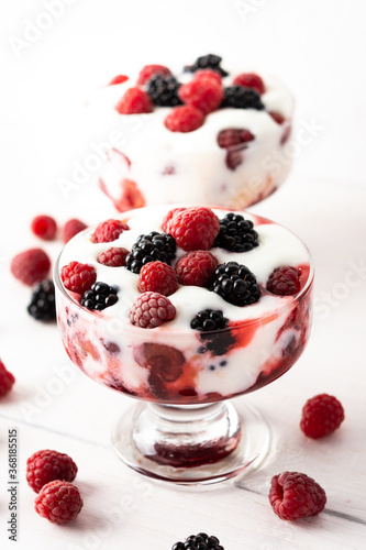Delicious juicy berries of raspberries and blackberries with yoghurt in a glass form on a white background