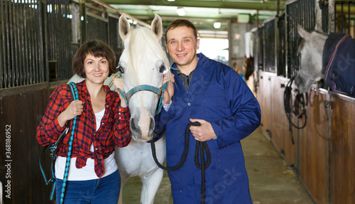 Happy man and woman in casual clothes at horse stable