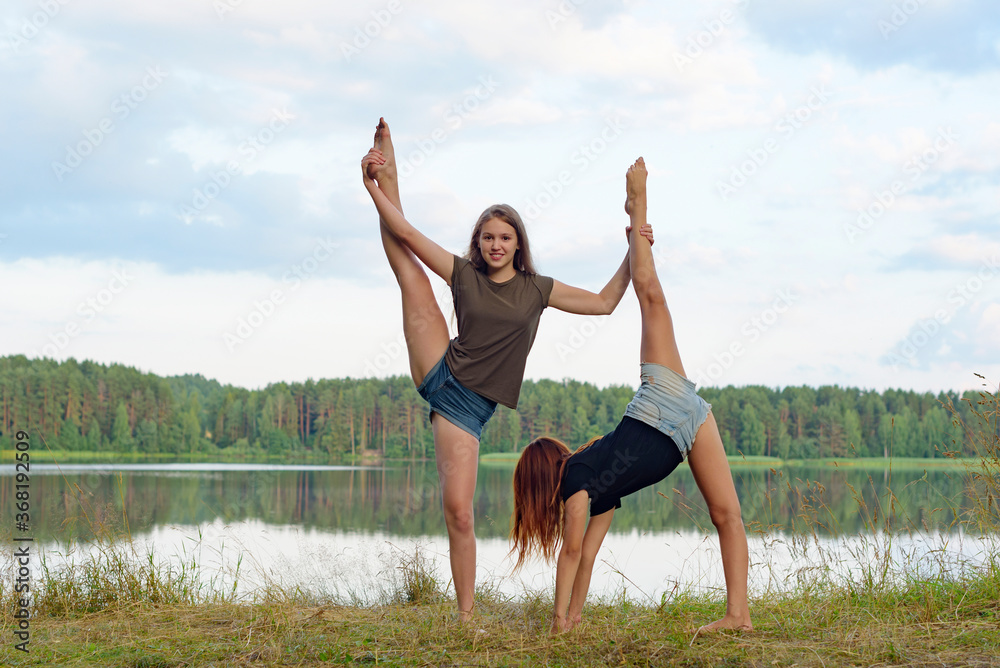 two girls do gymnastic exercises outdoor in a picturesque place by the river and having fun two girls do gymnastic exercises outdoor in a picturesque place by the river and having fun