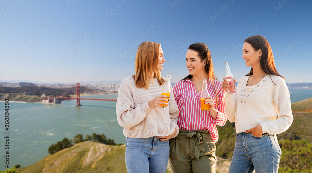 travel, tourism and friendship concept - group of happy young women or female friends with non alcoholic drinks talking over golden gate bridge in san francisco bay background