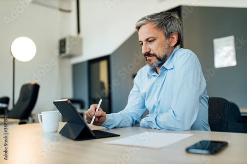 Close-up portrait of a mature businessman working on digital tablet.