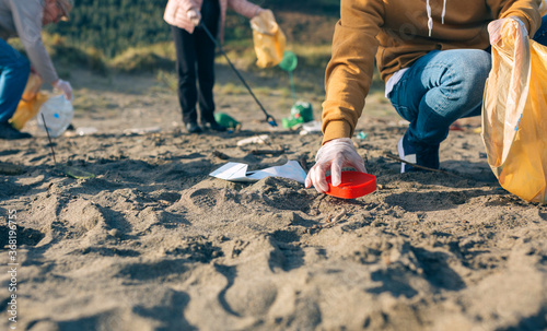Unrecognizable young man picking up trash with group of volunteers on the beach