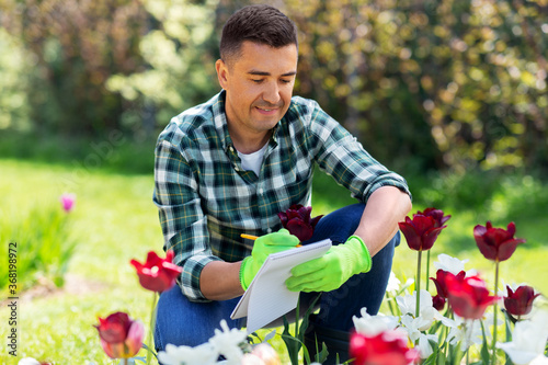 gardening and people concept - happy smiling middle-aged man writing to notebook and taking care of flowers at summer garden © Syda Productions