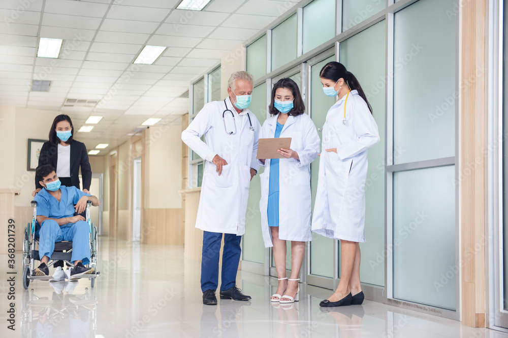 Obraz premium Female pushing patient man on wheelchair with three doctor talking in hospital corridor. health care, reanimation and medicine concept