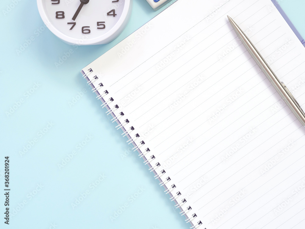 Blank notebook and pen with clock at 7:00 am, on blue work place desk table. Top view with space for text. Flat lay, Business and education concept... Blank notebook and pen with clock at 7:00 am, on blue work place desk table. Top view with space for text. Flat lay, Business and education concept...