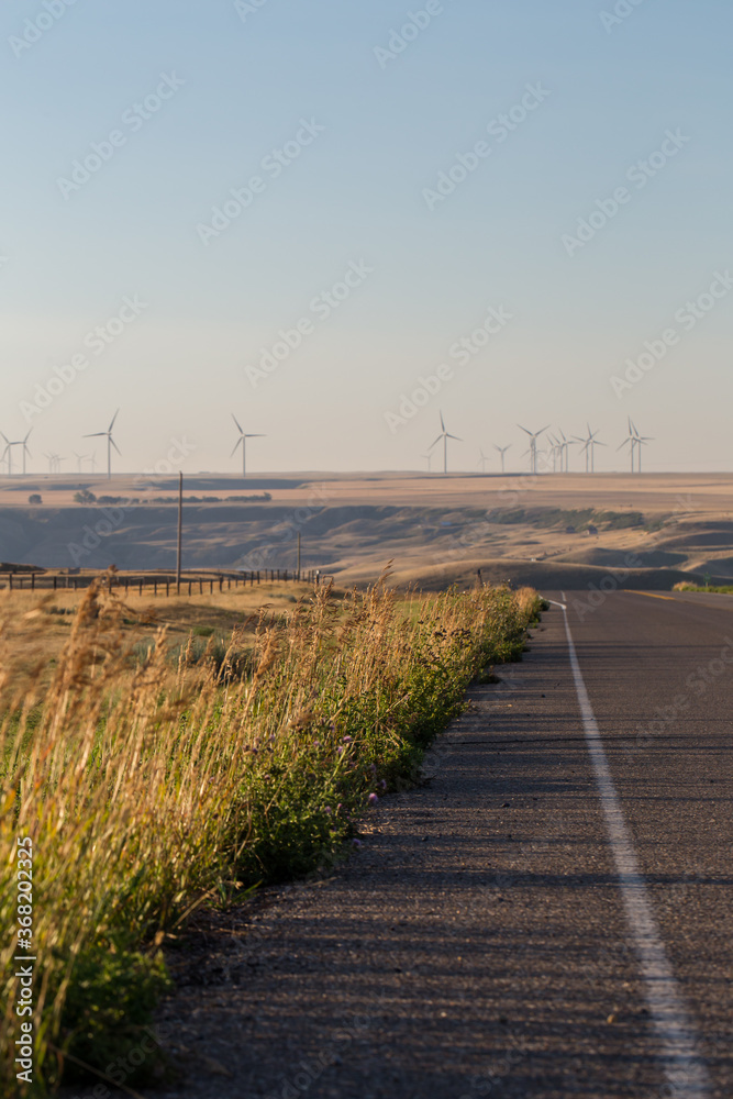 Windmill in the distance in Alberta Prairies. Wind farm power as an alternative energy source in front of a highway.Energy development and power generation. Wind Turbines and power generation.