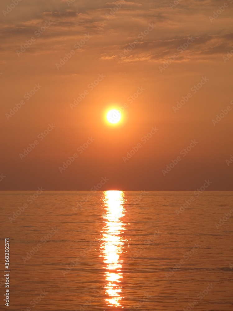 Scenic view of the bright golden setting sun and reflection in the sea water, sunset at the seaside, clouds, sky, sea and sun in bronze-orange-yellow tones