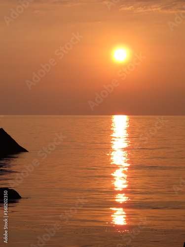 Seascape sunset on the sea coast, warm bronze-orange color of water, sky and sun, bright sunny path on the water surface 