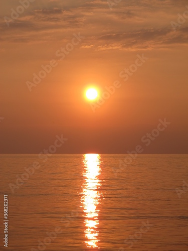 Scenic view of the bright golden setting sun and reflection in the sea water, sunset at the seaside, clouds, sky, sea and sun in bronze-orange-yellow tones © Vasilisa