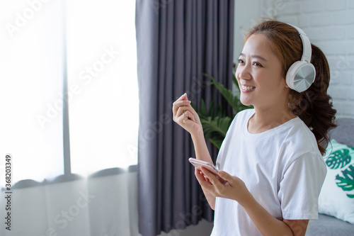 Asian woman was listening to music and singing a melody in the living room. She is very happy.