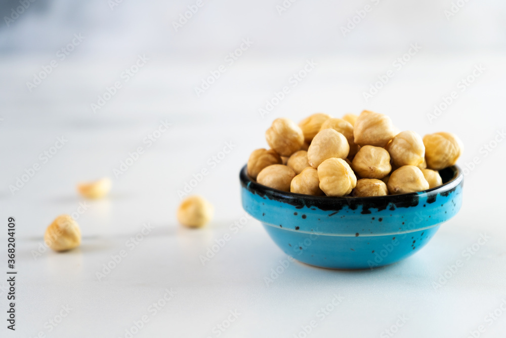 Peeled roasted hazelnuts in a blue round ceramic bowl stands on a white plate. Healthy and wholesome food high in protein, omega-3, antioxidants, minerals and vitamins. Close-up Peeled roasted hazelnuts in a blue round ceramic bowl stands on a white plate. Healthy and wholesome food high in protein, omega-3, antioxidants, minerals and vitamins. Close-up