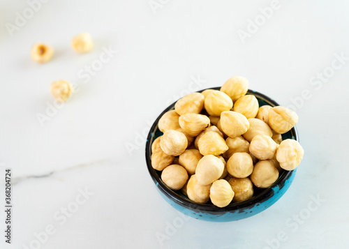 Hazelnuts in a blue bowl stands on a white plate. Delicious peeled hazelnuts. Healthy food, healthy snacks. Eating a handful of nuts a day can prevent various diseases. Top view, close-up