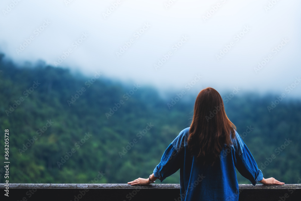Rear view image of a female traveler looking at a beautiful green mountain on foggy day