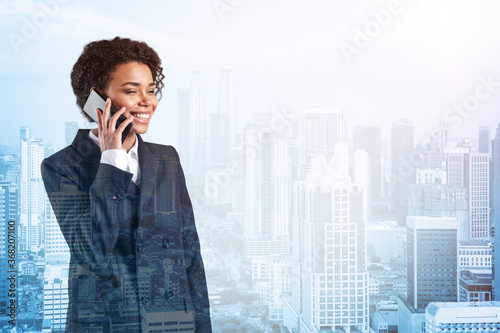 Successful smiling black African American business woman in suit pensively talking phone, Kuala Lumpur cityscape. The concept of consultants as problem solvers. KL skyscrapers. Double exposure. photo