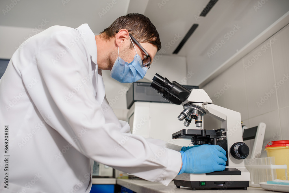 In the hospital laboratories working process, a young man doctor is looking in the medical microscope In the hospital laboratories working process, a young man doctor is looking in the medical microscope