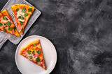 Hot pizza slices with mozzarella cheese, ham, tomato and parsley on wooden cutting board and plate, stone concrete background, top view copy space for text