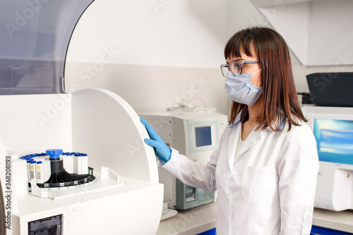Fototapeta Naklejka Na Ścianę i Meble -  In the hospital laboratory working process, a young woman laboratory assistant is turning on fully-automated diagnostic chemistry system