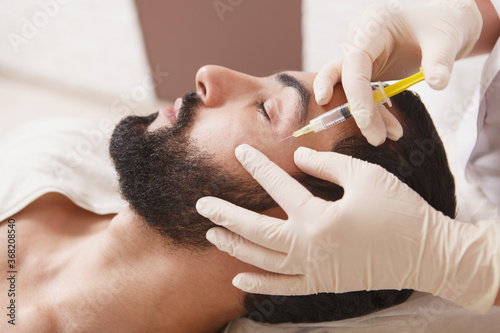 Bearded man getting anti-wrinkle face filler treatment by beautician