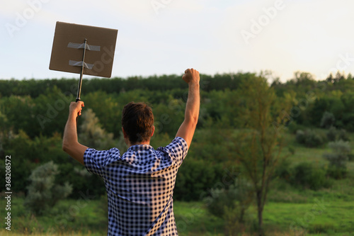 Man walkst hrough the park to protest. In his hand he holds a periscopic baton to which a cardboard plaque is attached photo