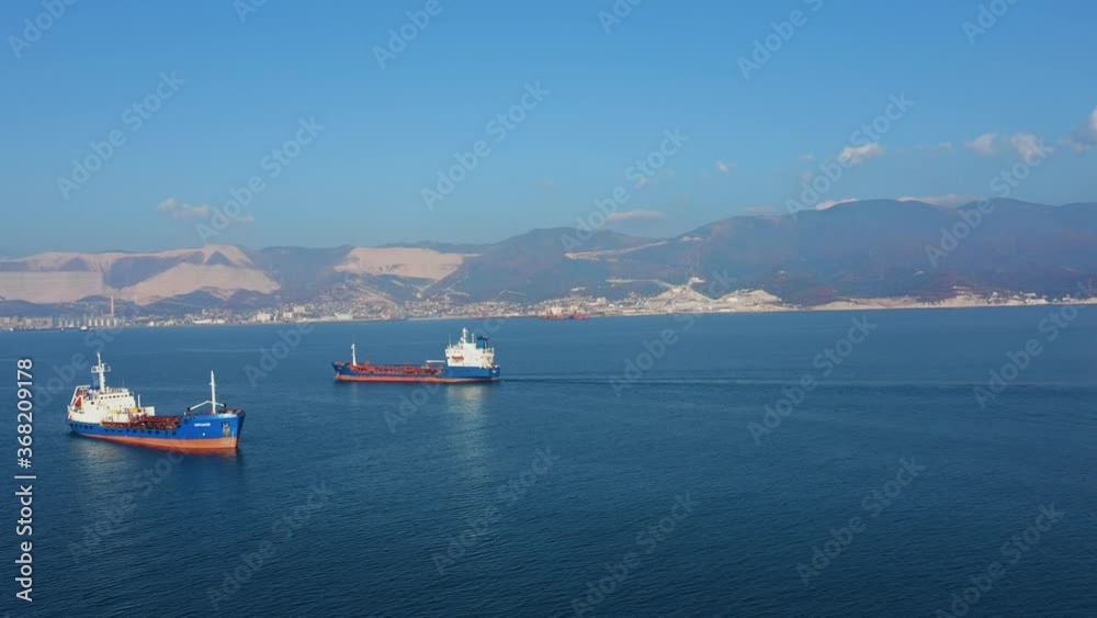 Aerial view of two large cargo ships leaving sea harbour at sunny day, mountains on background. Top down drone footage of tanker view from above. Concept of transport logistics, maritime Aerial view of two large cargo ships leaving sea harbour at sunny day, mountains on background. Top down drone footage of tanker view from above. Concept of transport logistics, maritime