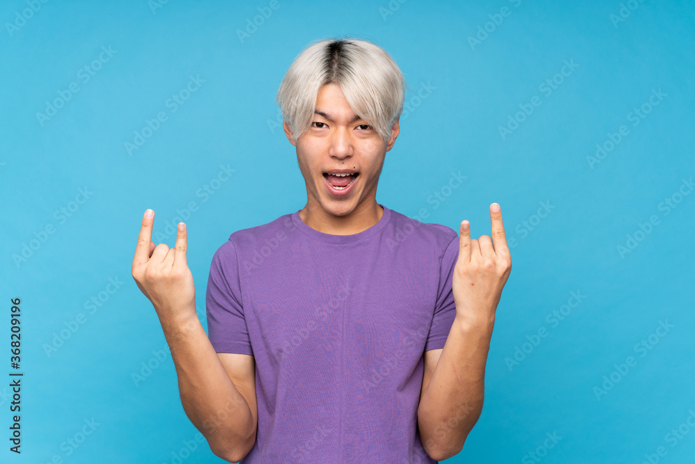 Young asian man over isolated blue background making rock gesture Young asian man over isolated blue background making rock gesture