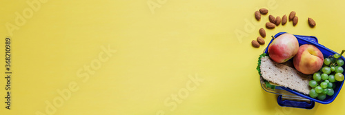 Large yellow background with school lunch with crispbreads with lettuce and cheese, apple, peach, grapes and almonds. Healthy school lunch. A healthy lunch box on a yellow background with free space.