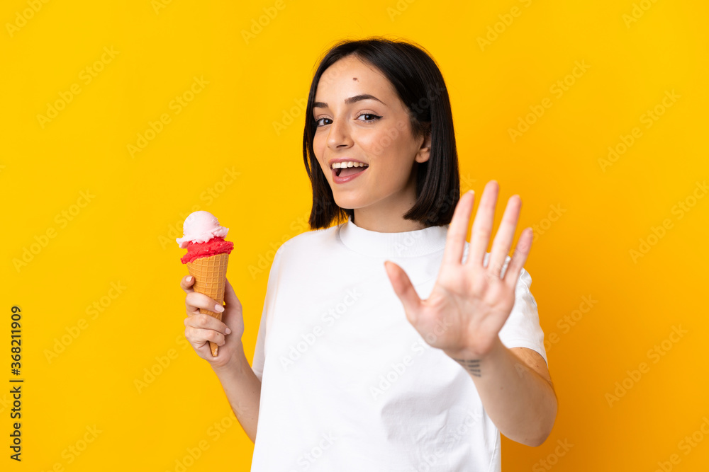 Young caucasian woman with a cornet ice cream isolated on yellow background saluting with hand with happy expression Young caucasian woman with a cornet ice cream isolated on yellow background saluting with hand with happy expression