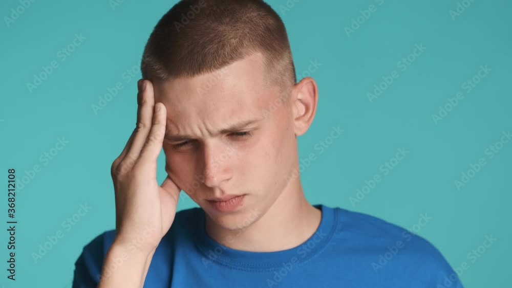 Portrait of upset blue eyed guy sadly  showing headache on camera over colorful background