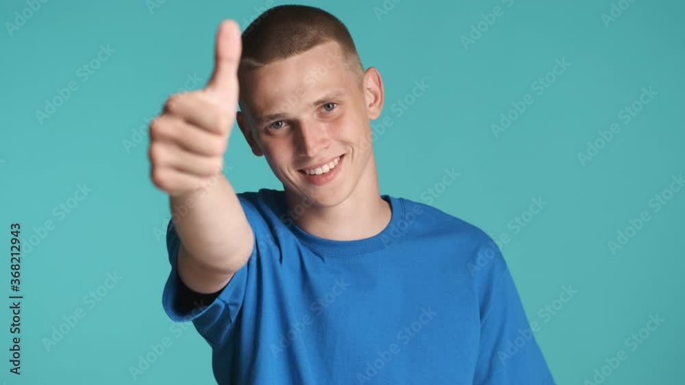 Attractive smiling blue eyed guy happily showing you and thumb up gestures on camera over colorful background Attractive smiling blue eyed guy happily showing you and thumb up gestures on camera over colorful background