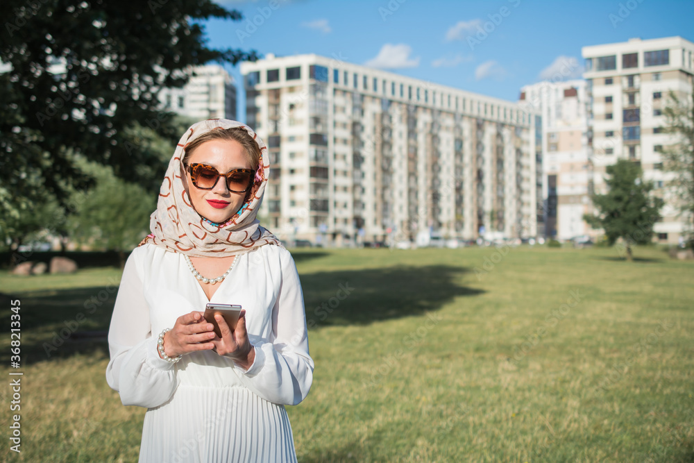 Fototapeta premium elegant girl in a white dress stands and reads a message on a smartphone