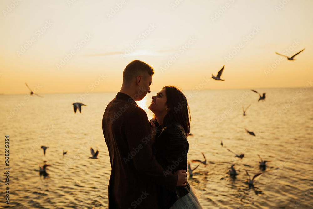 Honeymoon happy romantic couple in love embracing on the beach on orange sunset background and flying seagulls, Happy young couple embracing enjoying sea sunset during travel. Copy space.