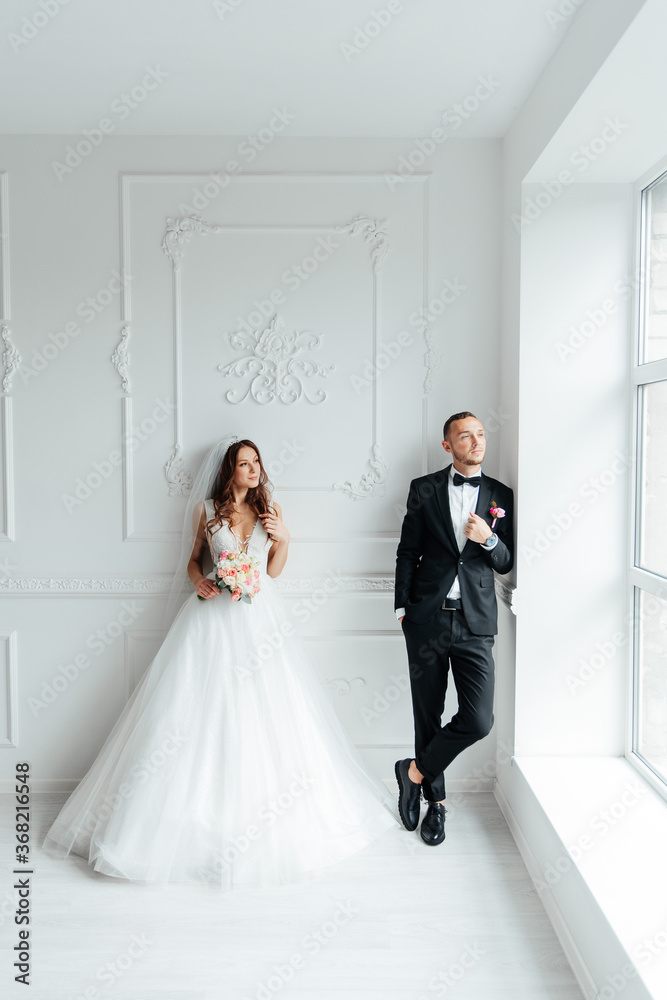 The first meeting of the groom in a black suit and the bride in a white wedding dress with a bouquet in the interior of a photo studio on a white and black background The first meeting of the groom in a black suit and the bride in a white wedding dress with a bouquet in the interior of a photo studio on a white and black background