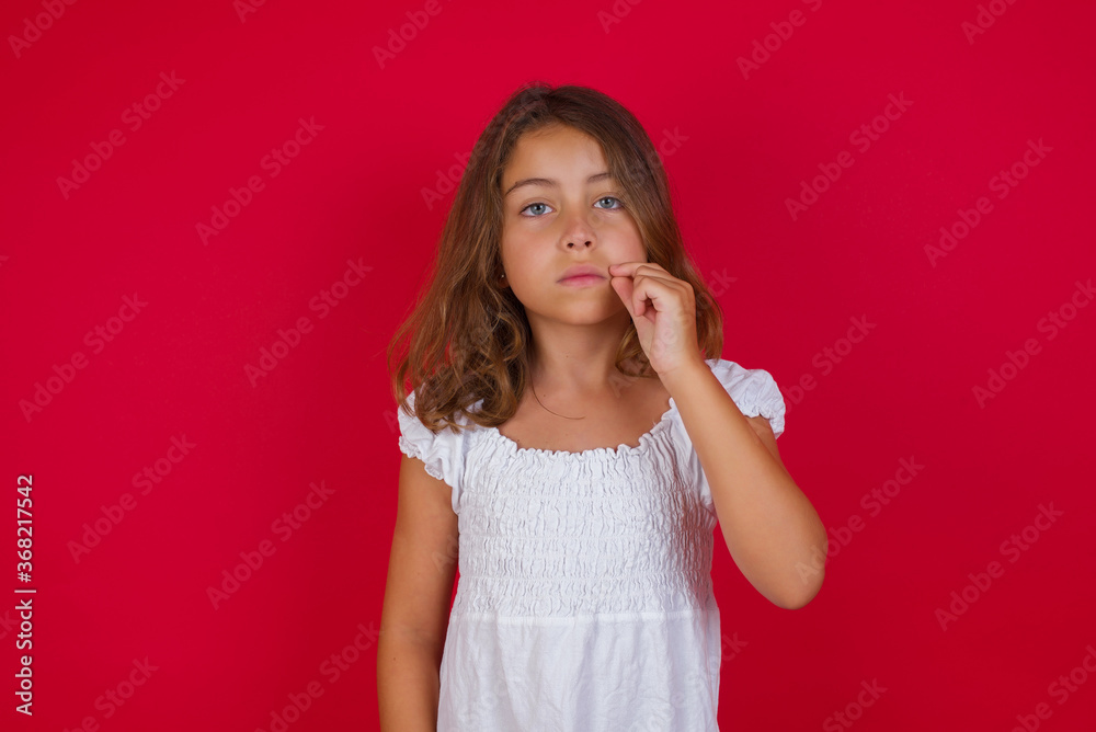 Little caucasian girl with blue eyes wearing white dress standing over isolated red background mouth and lips shut as zip with fingers. Secret and silent, taboo talking. Little caucasian girl with blue eyes wearing white dress standing over isolated red background mouth and lips shut as zip with fingers. Secret and silent, taboo talking.