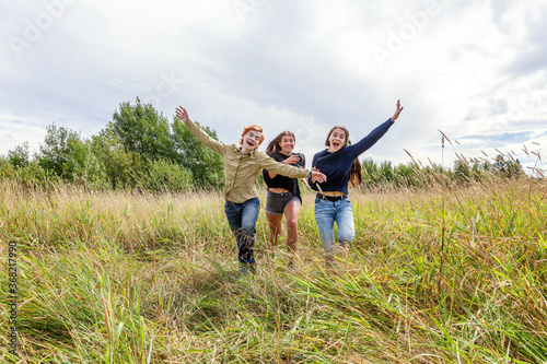 Summer holidays vacation happy people concept. Group of three friends boy and two girls running and having fun together outdoors. Picnic with friends on road trip in nature.