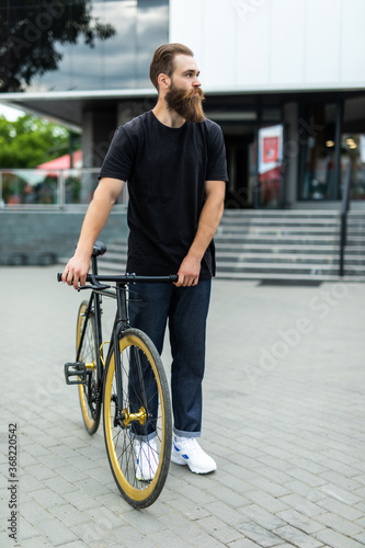 Enjoying the urban lifestyle. Young bearded man near his bicycle outdoors