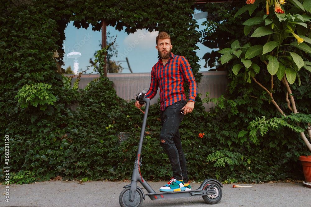 Full length of handsome young bearded caucasian man with sunglasses rides on the street e scooter Full length of handsome young bearded caucasian man with sunglasses rides on the street e scooter