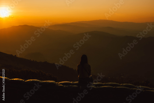 Silhouette of a girl sitting on a cliff side looking at the sunset. Beautiful sunset background.